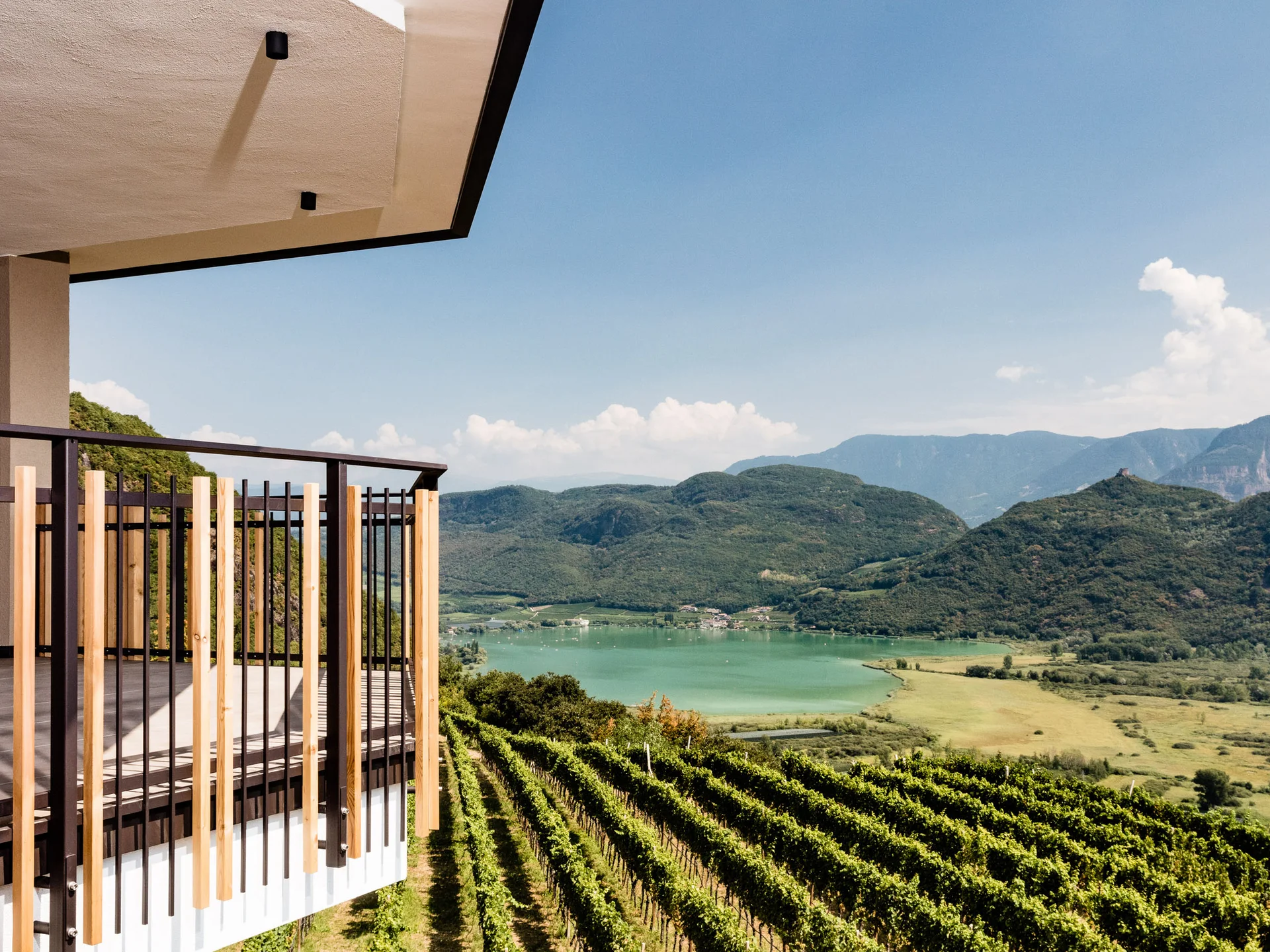 Ihr Hotel in Tramin: ein Genussort inmitten der Weinberge Balkon mit Blick auf Weinberg, See und Berge unter blauem Himmel
