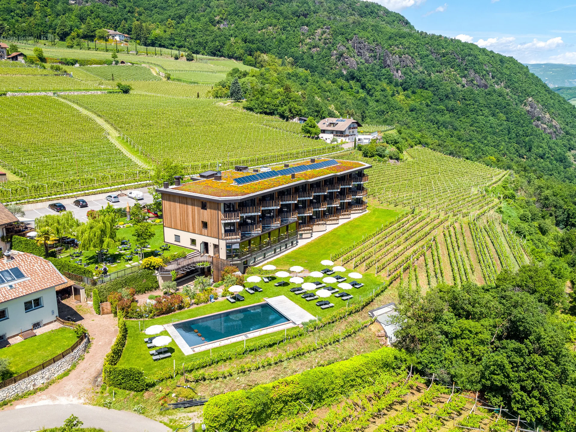 Ihr Hotel in Tramin: ein Genussort inmitten der Weinberge Hotel mit Pool und Sonnenschirmen inmitten von Weinbergen und Bergen