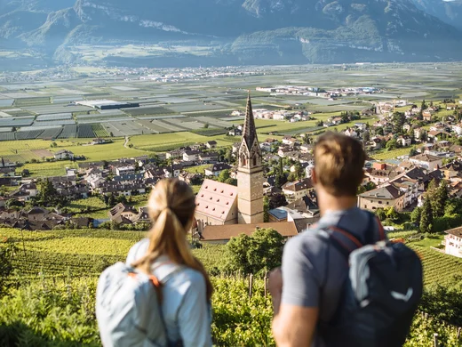 Ihr Hotel in Tramin: ein Genussort inmitten der Weinberge Zwei Wanderer blicken auf Dorf mit Kirche und Berge im Hintergrund