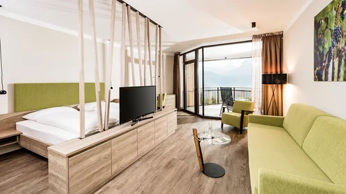 Ihr Hotel in Tramin: ein Genussort inmitten der Weinberge Modernes Hotelzimmer mit grünem Sofa, Bett und Balkon mit Bergblick