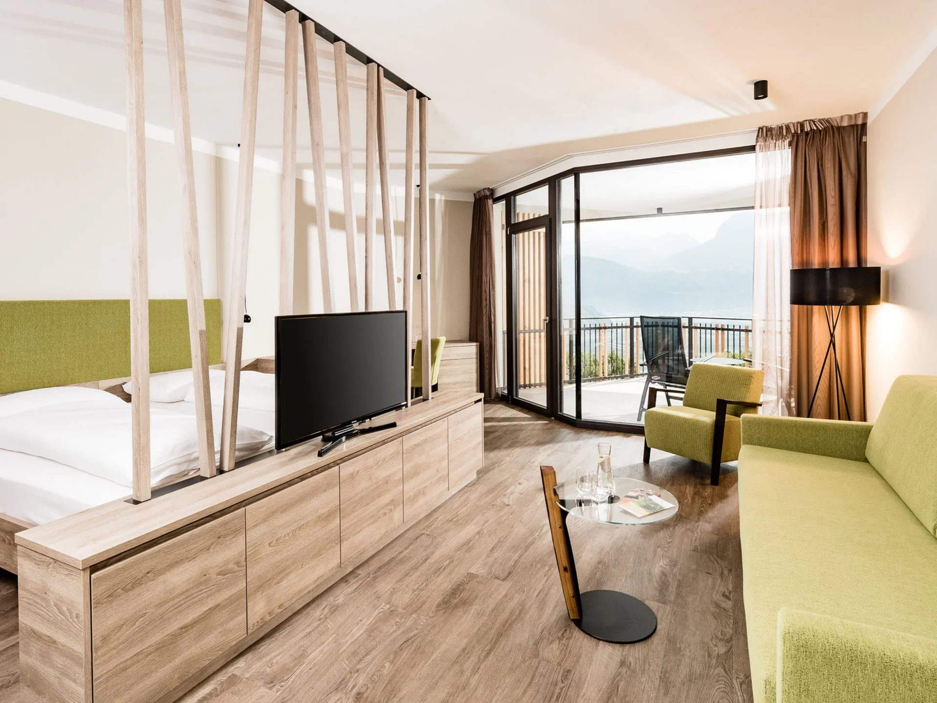 Ihr Hotel in Tramin: ein Genussort inmitten der Weinberge Modernes Hotelzimmer mit grünem Sofa, Bett und Balkon mit Bergblick