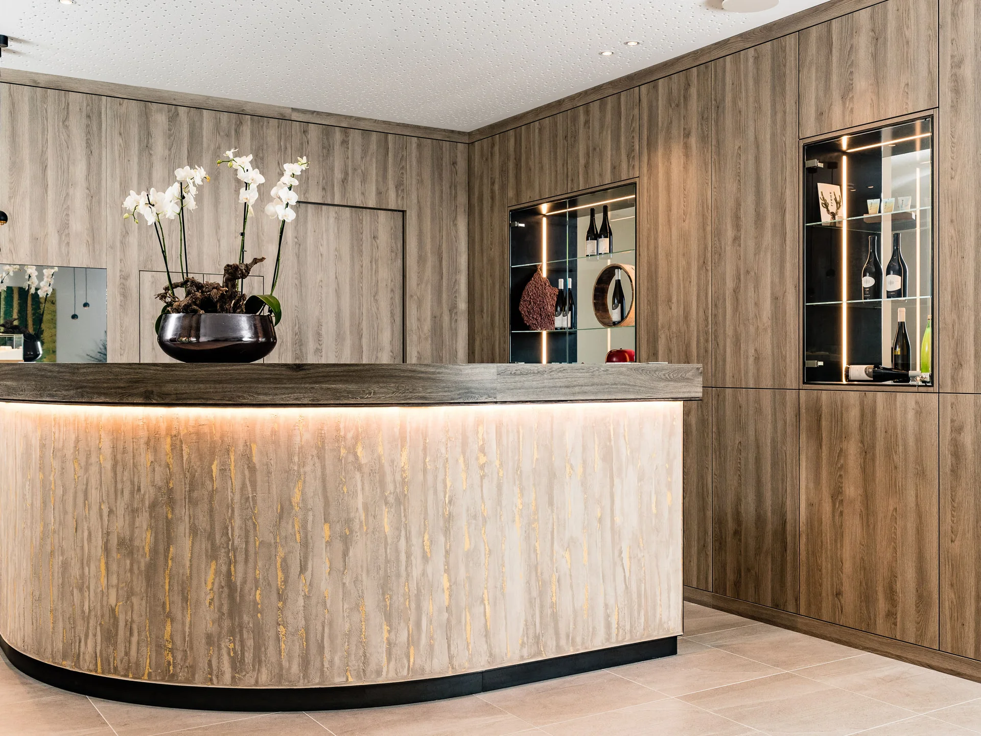 Ihr Hotel in Tramin: ein Genussort inmitten der Weinberge Moderner Empfangstresen mit Orchideen und Holzwandverkleidung