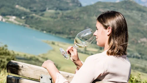 Ihr Hotel in Tramin: ein Genussort inmitten der Weinberge Frau genießt ein Glas Weißwein mit Blick auf See und Berge