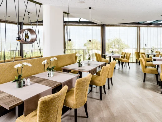 Il vostro ristorante a Termeno: cucina altoatesina e pizza Ristorante luminoso con sedie gialle e tavoli decorati con fiori su runner.