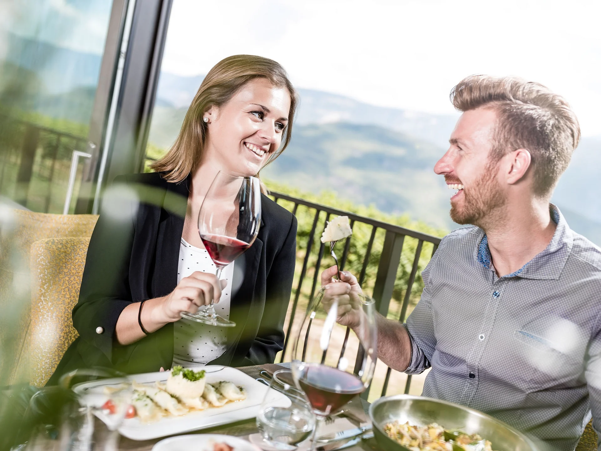 Ihr Hotel in Tramin: ein Genussort inmitten der Weinberge Paar genießt Wein und Essen auf Terrasse mit Bergblick