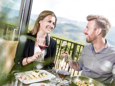 Ihr Hotel in Tramin: ein Genussort inmitten der Weinberge Paar genießt Wein und Essen auf Terrasse mit Bergblick