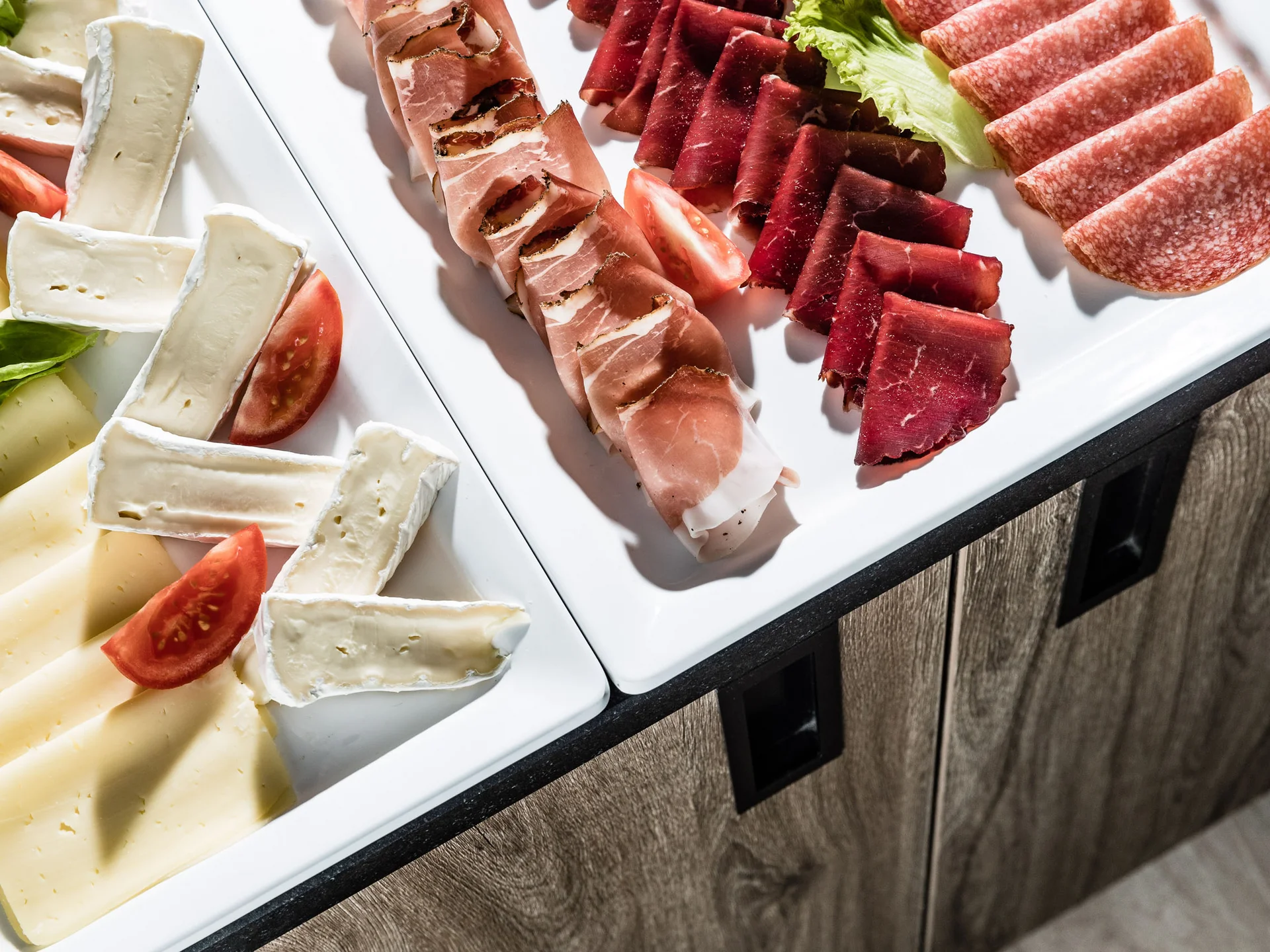 Ihr Hotel in Tramin: ein Genussort inmitten der Weinberge Verschiedene Käsesorten und Aufschnitt auf weißen Tellern mit Tomaten und Salat