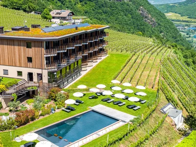 Ihr Hotel in Tramin: ein Genussort inmitten der Weinberge Hotel mit Pool und Sonnenschirmen zwischen Weinbergen in hügeliger Landschaft